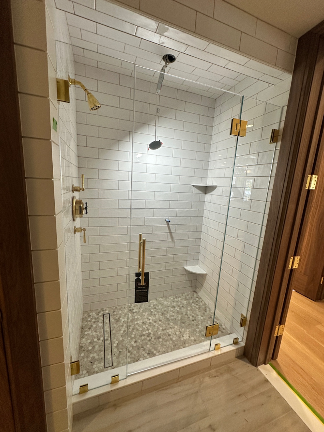 Frameless shower door with brushed gold hardware on white subway tile