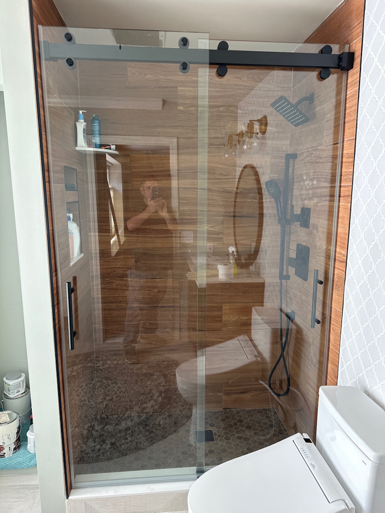 Matte black sliding barn-style glass shower door on wood-look tile